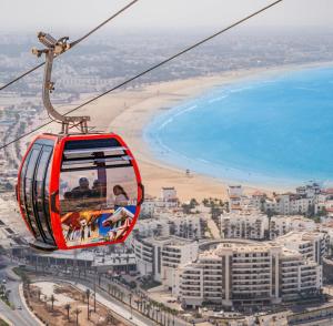 a gondola ride over the beach in front of a city at S1 Modern & Relax in Agadir