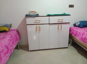 a room with a white cabinet and two beds at Dar Calme Takad in Ben Guemoud