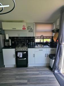 a kitchen with white cabinets and a sink and a stove at Lownie lodge in Leysdown-on-Sea +10 photos