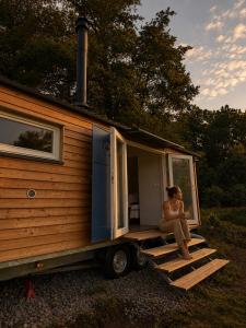 a woman sitting on the back of a tiny house at maringotka Hedvika glamping in Pašice