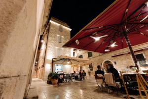 a group of people sitting at tables under a red umbrella at Murum Heritage Hotel in Split