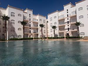 a swimming pool in front of a building with palm trees at Appartement avec piscine, résidence assadaka in Saïdia