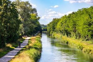 a river with trees and a person walking along it at Les Gîtes du Chemin - La Colombière in Paray-le-Monial