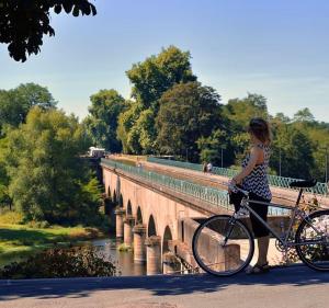 a woman standing with a bike on a bridge at Les Gîtes du Chemin - La Colombière in Paray-le-Monial
