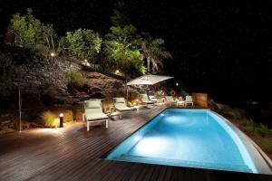 a swimming pool with chairs and an umbrella at night at Massapez Royals in Fajã da Ovelha