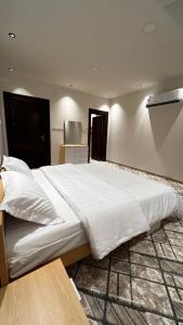 a large white bed in a room with a table at شالية بمسبح وجلسة خارجية- غرفتين نوم وملحق خارجي ومدخل سيارة in Unayzah