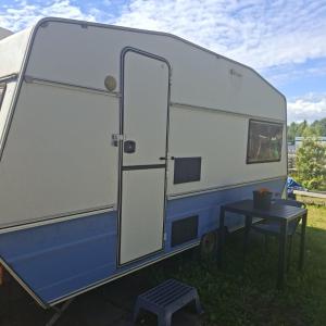 a white and blue trailer with a table in the grass at Cozy Caravan With House Access! in Luleå