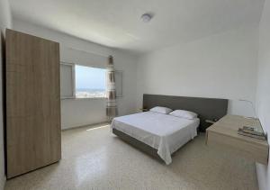 a white bedroom with a bed and a window at Soltane Résidence in Hammamet