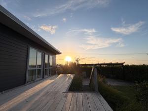 a wooden deck with the sun setting behind a house at Black Box Bach in Coopers Beach +14 photos