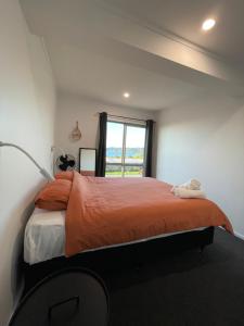 a bedroom with a bed with an orange comforter and a window at Black Box Bach in Coopers Beach