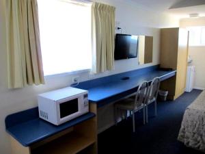 a room with a desk with a microwave and a television at Merimbula Coastline Motel in Merimbula