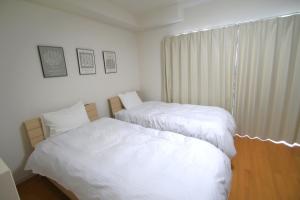 two beds in a room with white sheets and a window at オンブラージュ704号室-無料駐車場付き-繁華街まで徒歩圏内-南向きで明るいワンルーム in Kumamoto
