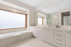 a white bathroom with a tub and a large window at 9 Doors From Front Beach in Point Lonsdale +12 photos