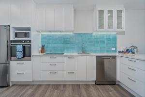 a white kitchen with white cabinets and blue tiles at Seaview Studio Apartment - Beachfront with Heated Pool in Whitianga