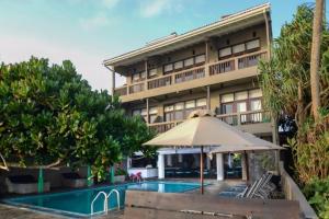 a hotel with an umbrella and a swimming pool at At Ease Beach Hotel in Hikkaduwa