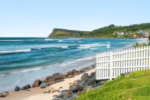 a beach with a white fence and the ocean at Apartment 4B in Lennox Head