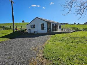 a small white house in a field with a fence at Rolling Hills Cottage in Tauwhare