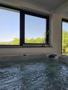 a bath tub in a room with two windows at Luni Stay - Jacuzzi, Sauna & Nature Escape in Jastrebarsko