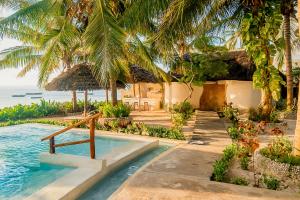 a resort swimming pool with palm trees and the ocean at Villa Juliana in Jambiani