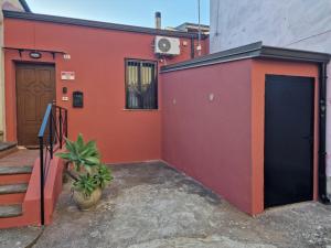 a red building with a door and a plant at Vicolo Stretto Guest House Centro storico in Vibo Valentia