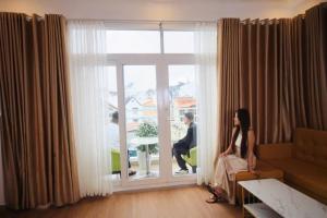 a woman sitting in a living room looking out the window at New Sun Hotel in Da Lat