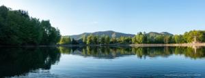 a large lake with trees and mountains in the background at CABANA BERNER stațiunea Mogoșa in Baia-Sprie