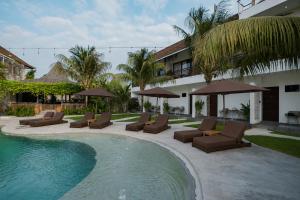 a pool with chairs and umbrellas next to a building at Suksma Guesthouse in Canggu