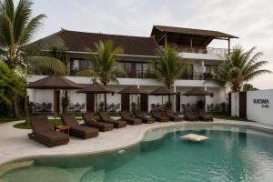 a hotel with a swimming pool with chairs and umbrellas at Suksma Guesthouse in Canggu