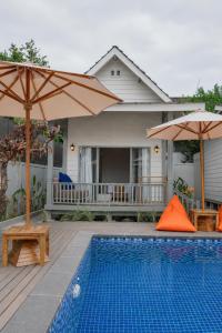 a swimming pool with two umbrellas and a house at Hu'u Beach Front Hotel in Gili Trawangan