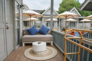 a porch with a couch and chairs and umbrellas at Hu'u Beach Front Hotel in Gili Trawangan