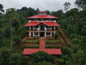 a house with a red roof in the middle of a forest at Naisarga hill view homestay in Somvārpet