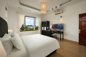 a white bedroom with a bed and a desk with a television at Maison Bay View Villa Cat Ba in Ðồng Khê Sâu