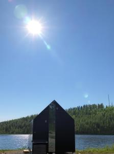 a black building on the shore of a lake at Sāmeland Retreat, Mirrored Glass Cabins, Swedish Lapland in Arvidsjaur +39 photos