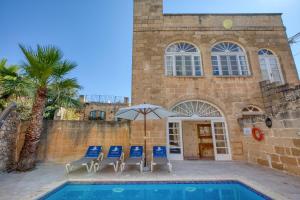 a pool with chairs and an umbrella next to a building at Kikka Holiday Home in Xagħra