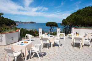 een terras met witte tafels en stoelen en uitzicht op de oceaan bij Hotel Punta Pina in Portoferraio