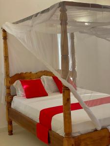 a bedroom with a canopy bed with red and white pillows at Ocean view in Watamu