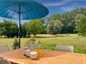 a wooden table with an umbrella and a field at L'Abri Côtier, maison spacieuse avec jardin in Pendé
