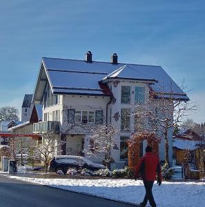 a man walking in front of a house in the snow at Eichkobel-Blick in Grünenbach