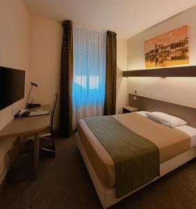 a hotel room with a bed and a desk and a television at Hôtel de La Cloche in Dole
