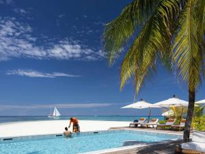 a man standing next to a swimming pool next to the beach at V Villas Maldives at Mirihi - MGallery Collection in Mandhoo