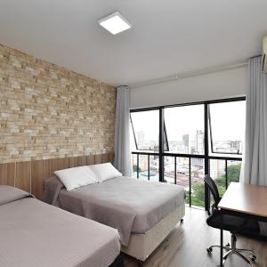 a bedroom with two beds and a desk and windows at Apart 1803 - Centro Curitiba in Curitiba