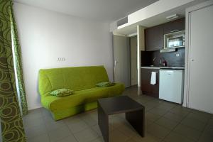 a living room with a green couch and a kitchen at KOSY Appart'Hôtels - Campus Del Sol Esplanade in Montfavet