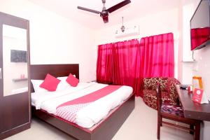 a bedroom with a bed and a desk and red curtains at Hotel O Dwarika Inn in Jabalpur