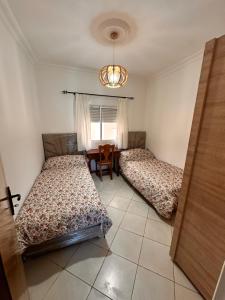 a bedroom with two beds and a table and a window at Appartement Nadin in Martil