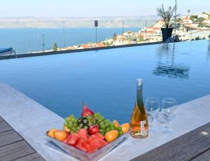 a plate of fruit and a bottle of wine next to a pool at חופש יהונתן-וילה סלביא עם נוף מטורף בריכה פרטית Hofesh Yehonatan Villa Selavi in Tiberias