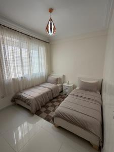 two beds in a white bedroom with a window at Superbe appartement pieds dans l’eau in Aourir +7 photos