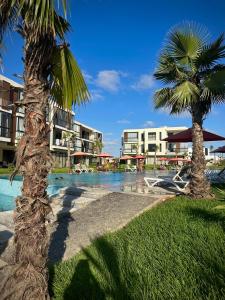 a resort swimming pool with palm trees and buildings at Relaxing residence oceanic Sidi rhal in Sidi Rahal