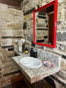 a bathroom sink with a red mirror on a stone wall at Chalé Carrara, um Refúgio de Pedra na Mata - Chalés Flor dos Manacás in Santa Teresa