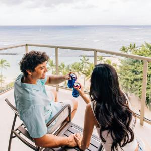 a man and a woman sitting on a balcony with the beach at Waikiki Circle Hotel by Castle in Honolulu