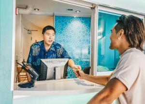 a woman standing in front of a mirror helping a man cut his hair at Waikiki Circle Hotel by Castle in Honolulu